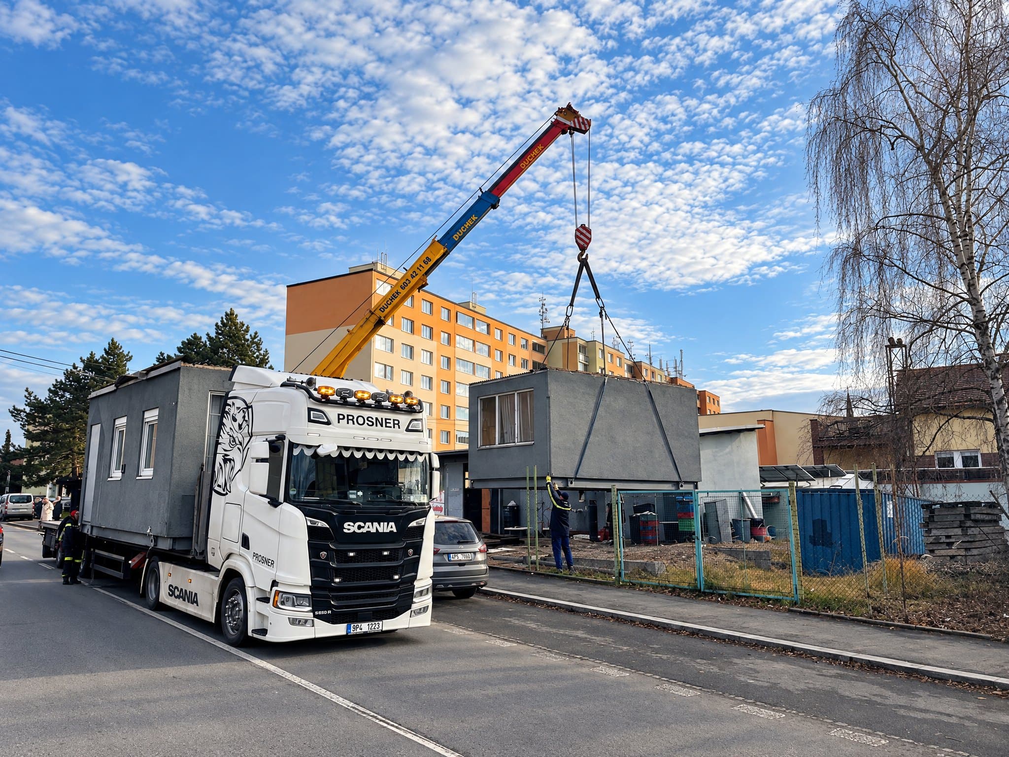 Autojeřáb zvedá modul stavby, v popředí tahač Scania PROSNER s dalším modulem